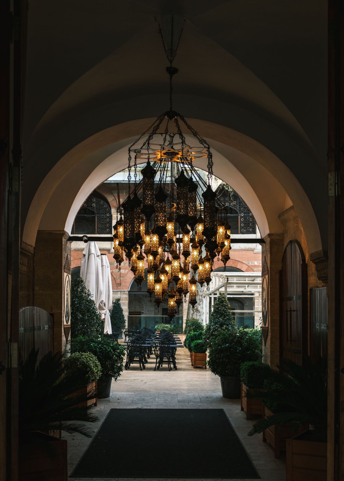 Patterned lantern cluster chandelier glowing beneath a stone archway facing an outdoor courtyard