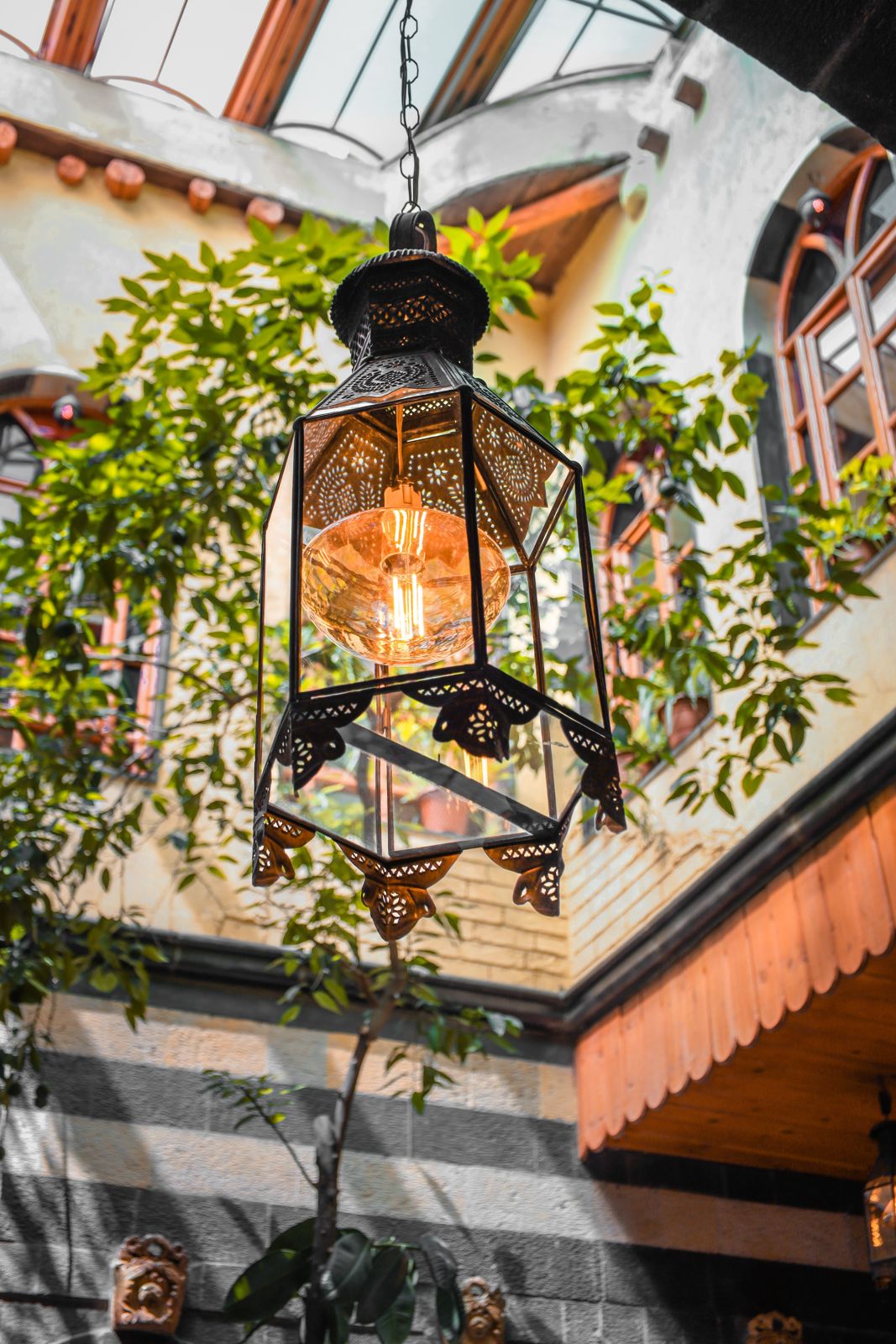 Pierced metal-look hanging lantern glowing in a leafy courtyard