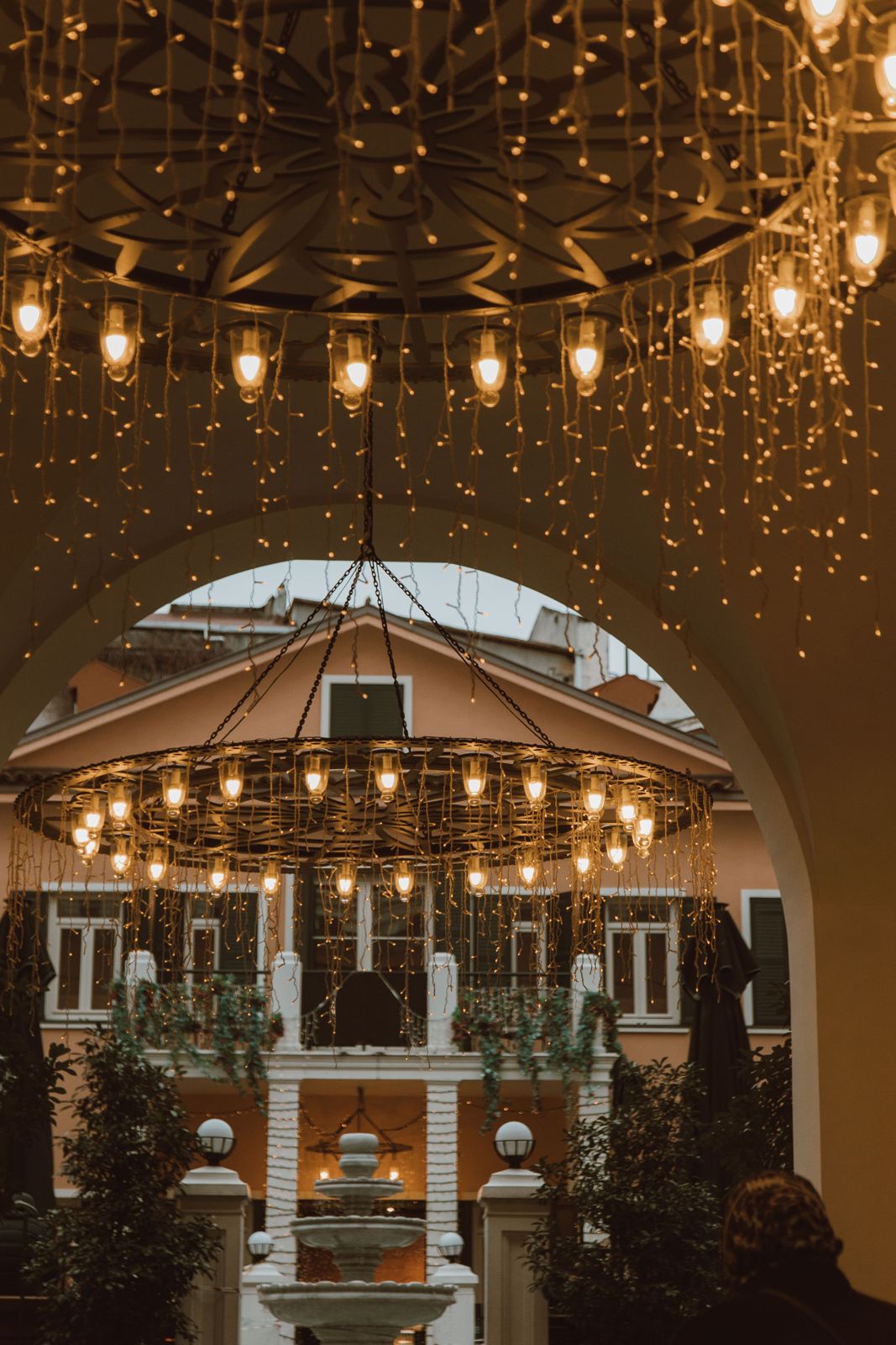 Fairy-light wheel chandelier glowing over a courtyard fountain